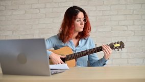 Woman learns to play guitar from video on laptop. Distance learning music in quarantine