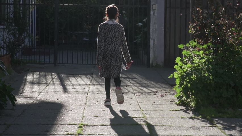 Slow motion of brunette girl walking towards the gate of her house at sunset