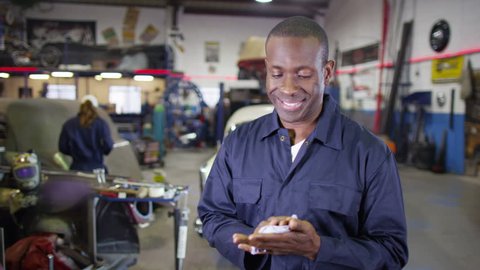4K Portrait of friendly smiling mechanic in garage workshop