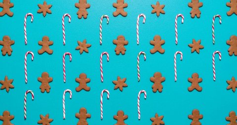Above view stop motion with cookies and candies arranged symmetrically and dancing on a blue table. Christmas sweets flat lay, gingerbread cookies and candy canes isolated on blue-colored background.