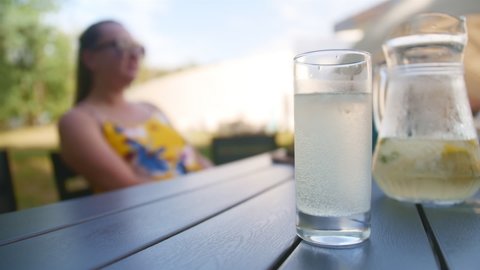 Close up of glass and jug of lemonade. Woman takes a glass of lemonade.