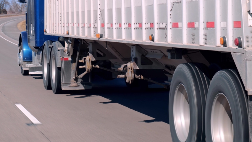 Semi truck and trailer driving on an American freeway on a sunny day, as seen through the windshield of a passing car. Royalty-Free Stock Footage #1062570589