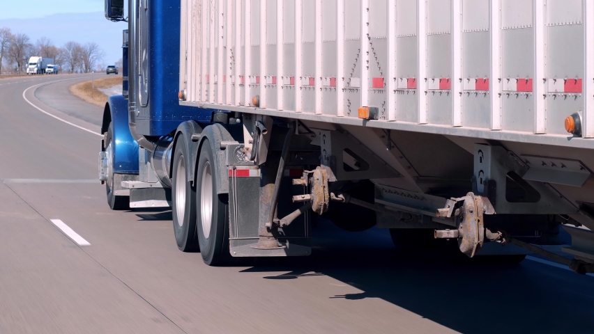 Semi truck and trailer driving on an American freeway on a sunny day, as seen through the windshield of a passing car.