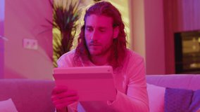 Young hipster caucasian man using digital tablet pc for online remote communication business interview job friend conversation online in neon lights.
