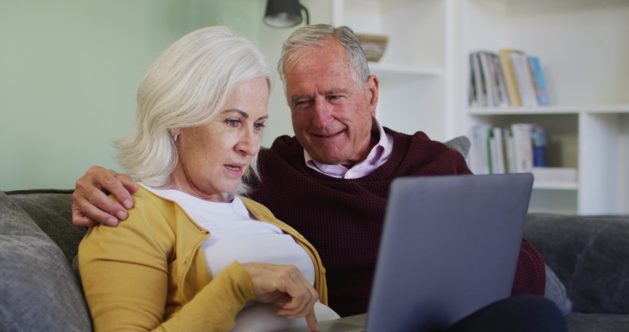 Senior caucasian couple using laptop computer together, smiling and talking at home sitting on sofa, in slow motion. quality time together at home during coronavirus covid 19 pandemic. | Shutterstock HD Video #1062575893