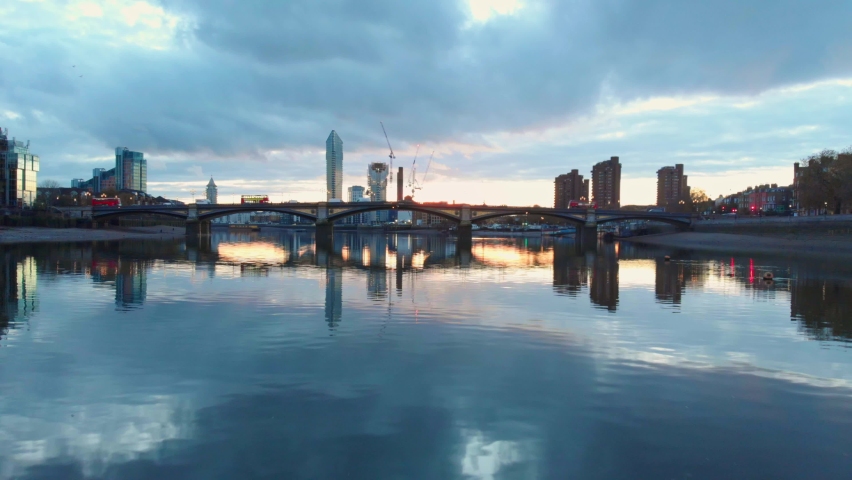 low drone shot of thames river traffic London bus on Battersea bridge and Chelsea harbour at sunset