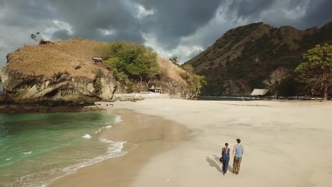 A couple walking on an idyllic Koka Beach. Hidden gem of Flores, Indonesia. Couple is enjoying their romantic escape. Waves gently washing the shore. There are hills in the back. Happiness and love
