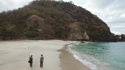 A couple walking on an idyllic Koka Beach. Hidden gem of Flores, Indonesia. Couple is enjoying their romantic escape. Waves gently washing the shore. There are hills in the back. Happiness and love
