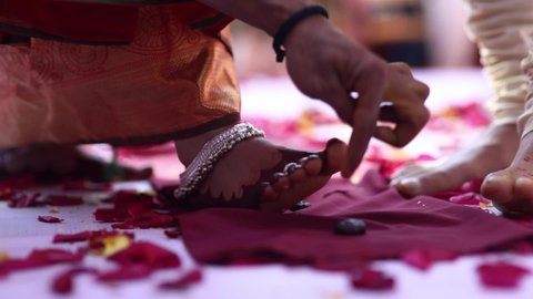 Priest hands supervising a traditional south indian wedding custom with bride and groom feet over flower petals on floor. Bride wearing silver anklet jewellery and body dye. day time temple marriage
