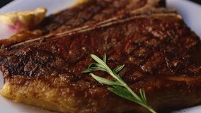 Huge t-bone steak grilled in restaurant.Delicious piece of beefsteak cooked on grill and served on white plate for dinner.Big chunk of beef meat on bone roasted on fire,filmed in close up video clip
