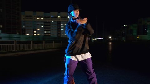 Cheerful young woman dancing hip hop, freestyle at night on a city street. Gimbal shot