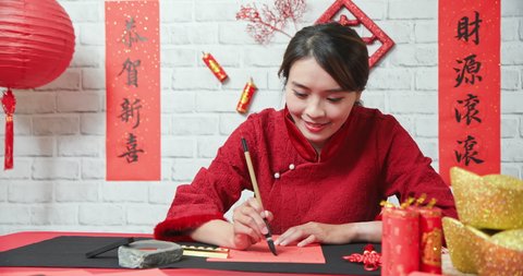 asian female writing spring festival couplets is celebrating Chinese holidays with word meaning new year and may wealth come generously to you
