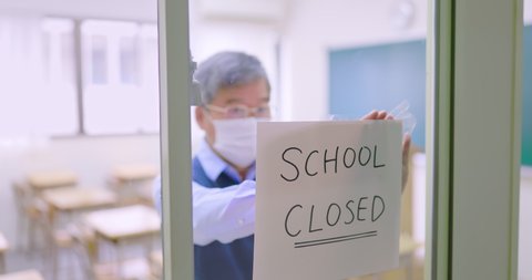 asian mature male professor put school closed sign on windows to prevent coronavirus spreading