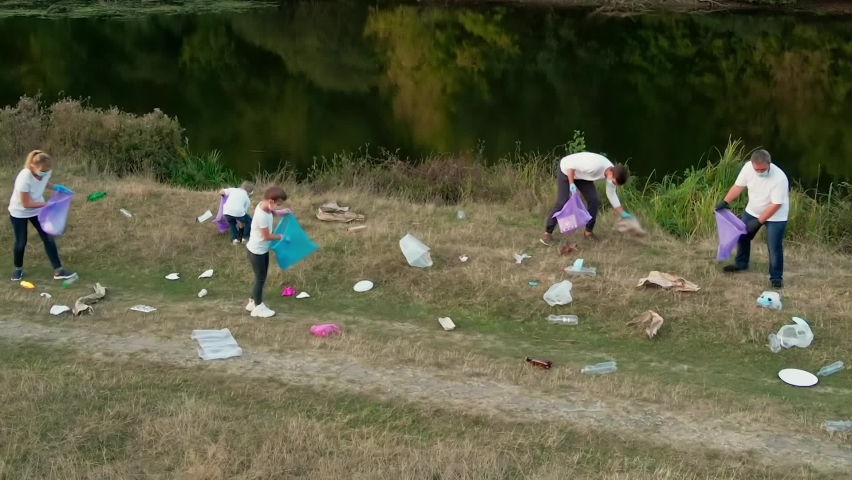 A family of volunteers with children clears the river Bank of garbage. People collect plastic leftovers in garbage bags. Environment, ecology, biosphere protection concept. | Shutterstock HD Video #1062599428