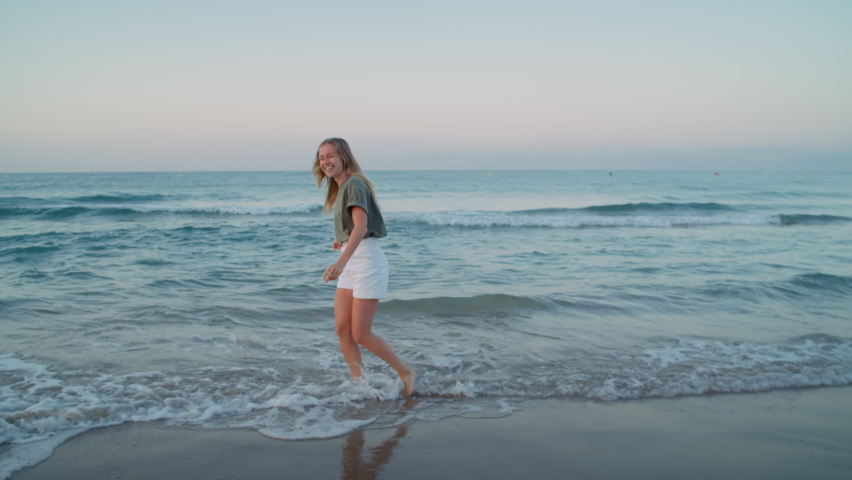 Authentic beautiful young woman dances happy in shoreline waves rolling over beach. Excited and happy, calm joyful pure happiness from being one with nature. Enjoy summertime vacation Royalty-Free Stock Footage #1062601987