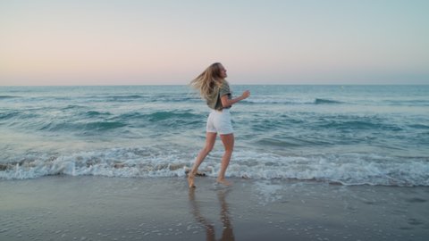 Authentic beautiful young woman dances happy in shoreline waves rolling over beach. Excited and happy, calm joyful pure happiness from being one with nature. Enjoy summertime vacation