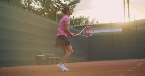 A young brunette tennis player plays a ball at sunset on a tennis court. A woman plays tennis professionally and dynamically in slow motion