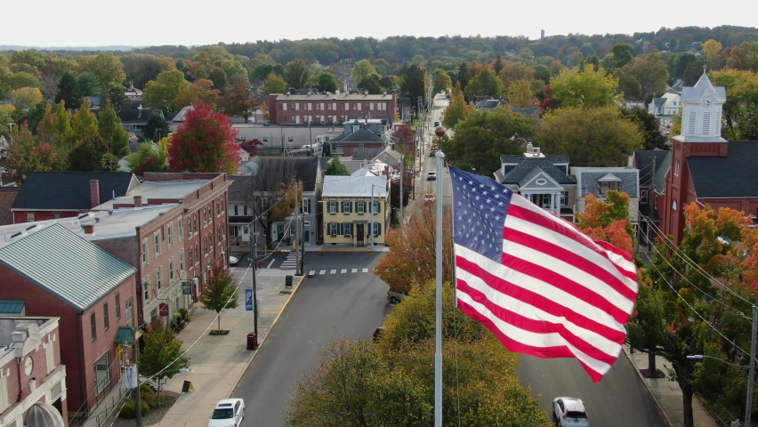 Patriotic American Flag flies over town square in Anytown USA. Beautiful cinematic aerial shot. Royalty-Free Stock Footage #1062615697