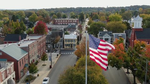 Patriotic American Flag flies over town square in Anytown USA. Beautiful cinematic aerial shot.