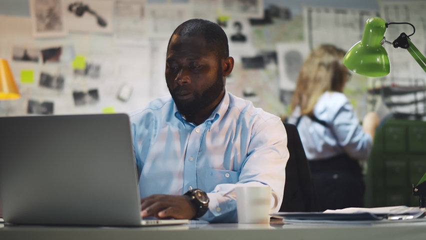 African detective processing evidence working on laptop in office. Portrait of serious afro-american police office sitting at desk and using computer at police station Royalty-Free Stock Footage #1062617806