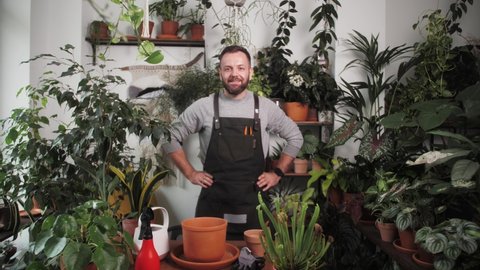 handsome young florist gardener portrait in greenhouse, man small business owner in flower shop, home interior store