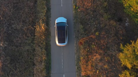 Aerial shot of electrical car driving through country road at summer evening. Modern vehicle passing rural highway. Ecology friendly car riding on electric charge along motorway. Top view