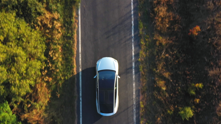 Aerial shot of electrical car driving on country road at summer evening. New SUV vehicle moving fast through highway. Ecology friendly auto riding on electric charge along motorway. Top view Royalty-Free Stock Footage #1062622186