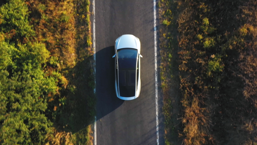 Aerial shot of electrical car driving on country road at summer evening. New SUV vehicle moving fast through highway. Ecology friendly auto riding on electric charge along motorway. Top view | Shutterstock HD Video #1062622186