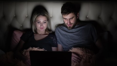 A man and a woman, a young couple watching a movie before going to bed in bed and emotionally discussing the plot