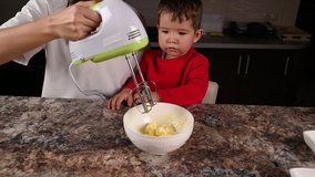 Mother and child stir the dough with a mixer. High quality video.