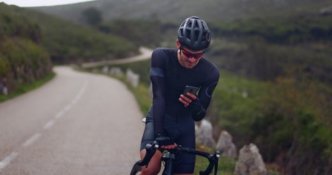 Professional cyclist checking smartphone on sports bicycle on a mountain