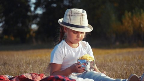 child eating chips close-up face. kid resting in the park eating chips. little girl resting on a picnic in the park eating potato chips. kid dream concept outdoor