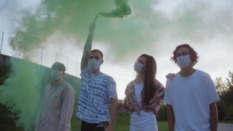 Group of happy friends having fun walking city streets with colorful smokes, wearing protection coronavirus covid 19 medical masks, young stylish millennials, Generation z youngsters, hip-hop punk