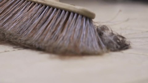 Close up on broom sweeping at hair salon, with hair cuttings fly in the air, slow motion low view