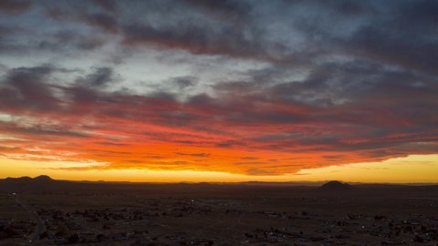 The desert sky cloudscape is illuminated by the setting sun with brilliant colors - aerial hyperlapse