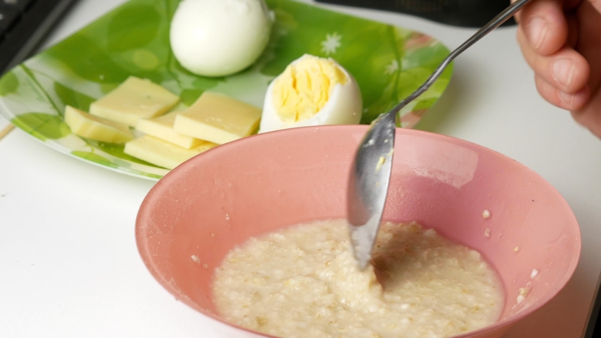 Breakfast for a healthy diet.Eats and mixes porridge with a spoon.Low-calorie foods.Chicken eggs and oatmeal.Pieces of milk cheese.A source of protein and carbohydrates.