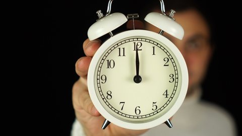 12 o'clock. Good morning or wake up concept. Human hand holding alarm clock that showing twelve o'clock and ringing.