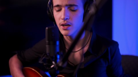 Young Boy sings and plays the electric guitar. Cinematic footage of teenager plays guitar at home. Young man plays a musical instrument. Musician in headset records his composition in a music studio. 