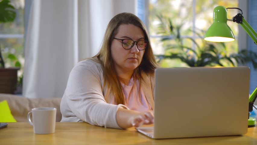 Tired fat woman suffering eyestrain working on laptop at home. Portrait of obese young female studying at home having migraine and massaging temples sitting at table with computer Royalty-Free Stock Footage #1062651442
