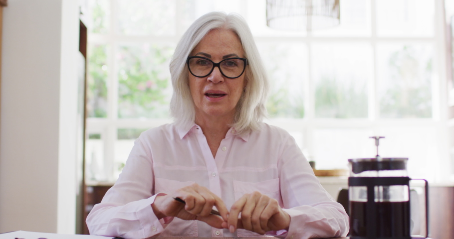 Portrait of senior woman wearing glasses talking looking at the camera while working from home. social distancing quarantine lockdown during coronavirus pandemic | Shutterstock HD Video #1062653044