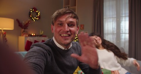 POV of cheerful Caucasian family man and woman with little daughter smiling and talking on video online in good mood in decorated house with glowing xmas tree on New Year's eve. Close up
