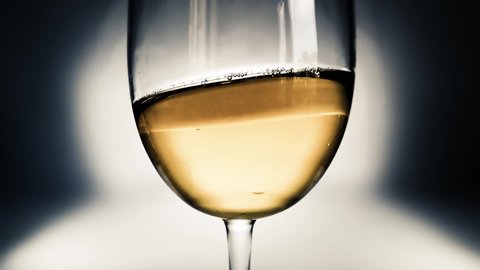 Creative macro slow motion video of white wine splashing in a glass from side to side like waves. Glass with splashing wine close-up. Old retro grunge vintage style.
