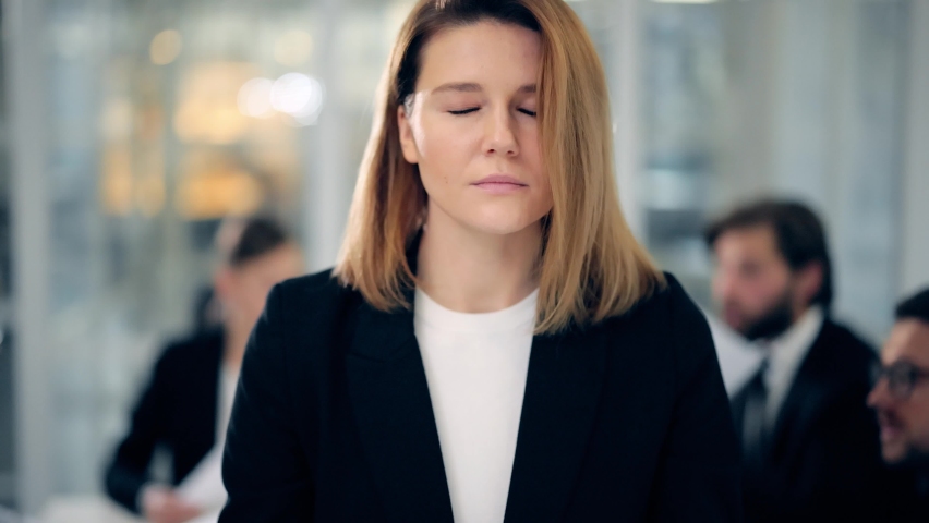 Calm blonde business woman dressed in classic black suit meditate in lotus position while office workers arguing and throwing papers to each other faces on business meeting at the background Royalty-Free Stock Footage #1062660502