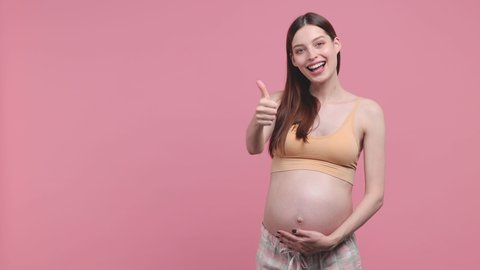 Happy young pregnant woman future mom in basic top stroking keep hands on belly tummy with baby pointing on workspace isolated on pink background studio. Maternity family pregnancy gynecology concept
