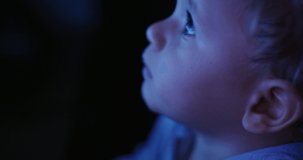 Cinematic macro shot of curious toddler baby boy eyes while watching television screen in the dark. Concept of technology, new generation, family, connection, vision of the future of children with web
