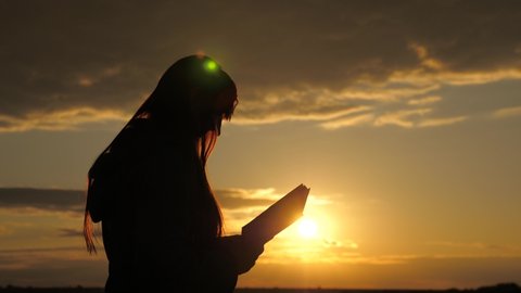 A woman reads a book in rays of the sun. Man reads Bible outdoors. A man holds Bible in his hands and studies the word of God at sunrise on top of mountain. Searching for truth in scriptures.