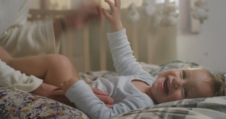 Cinematic close up shot of young happy mother is tickling and playing with her toddler baby boy in a nursery woke up in a morning. Concept of love, parenthood, childhood, life, maternity, motherhood. Royalty-Free Stock Footage #1062663103
