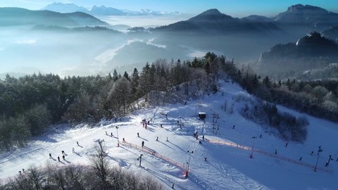 Aerial view of ski slope and skiers skiing down the slope. Beautiful ski resort with ski lifts and winter scenery with fresh white snow. Sunny day during winter holidays. Perfect ski conditions.