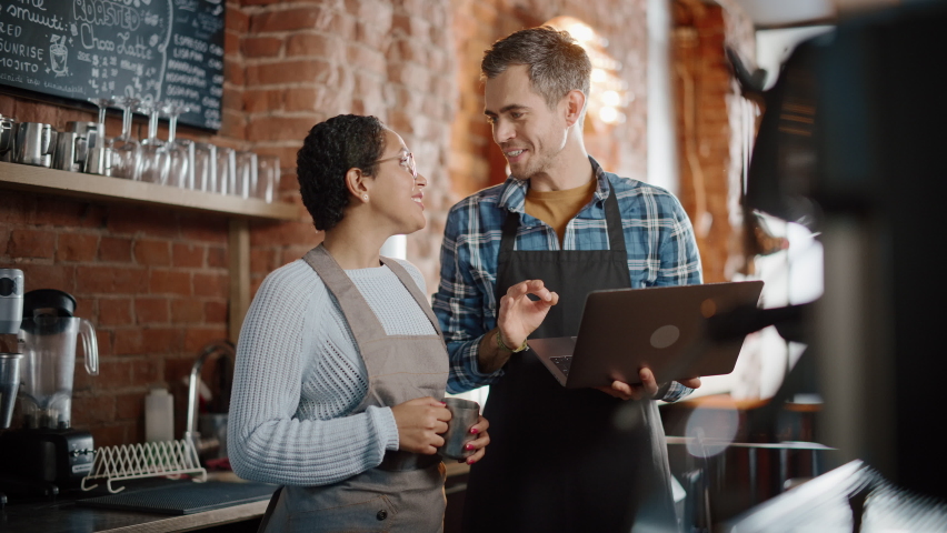 Two Diverse Entrepreneurs Have a Team Meeting in Their Stylish Coffee Shop. Barista and Cafe Owner Discuss Work Schedule and Menu on Laptop Computer. Multiethnic Female and Male Restaurant Employees. Royalty-Free Stock Footage #1062664294