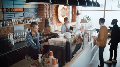 Latin Female Cashier and Male Barista in Checkered Shirt Accept Orders from Diverse Clients in Coffee Shop Bar. African American Handsome Customer Orders Take Away Latte from a Cozy Lifestyle Cafe.